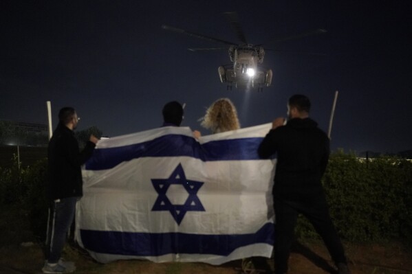 CAPTION CORRECTION CORRECTS LOCATION: People holding an Israeli flag watch the arrival of a helicopter transporting Israeli hostages released by Hamas at the Sheba Medical Center in Ramat Gan, Israel, Tuesday Nov. 28, 2023. Hamas and Israel released more hostages and prisoners under terms of a fragile cease-fire that held for a fifth day Tuesday. (AP Photo/Leo Correa)