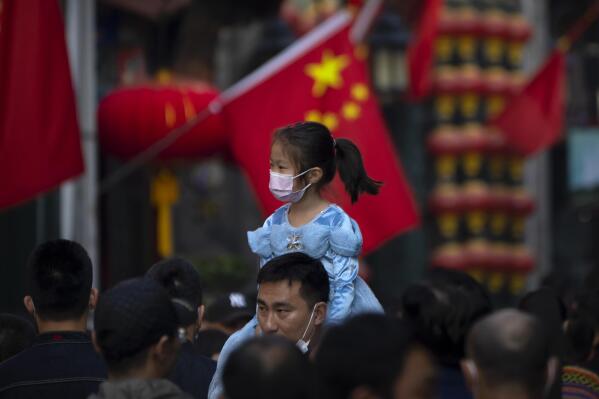 FILE - A girl wearing a face mask rides on a man's shoulders as they walk along a tourist shopping street in Beijing on Oct. 7, 2022. China has announced its first overall population decline in recent years amid an aging society and plunging birthrate. (AP Photo/Mark Schiefelbein, File)