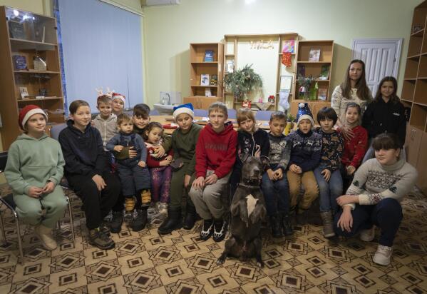 Children traumatized by the war pose for photo with an American Pit Bull Terrier "Bice" in the Center for Social and Psychological Rehabilitation in Boyarka close Kyiv, Ukraine, Wednesday, Dec. 7, 2022. Bice is an American pit bull terrier with an important and sensitive job in Ukraine — comforting children traumatized by the war. The Center for Social and Psychological Rehabilitation is a state-operated community center where a group of people are trying to help those who have experienced a trauma after the Feb. 24 Russian invasion, and now they are using dogs like Bice to give comfort. (AP Photo/Vasilisa Stepanenko)