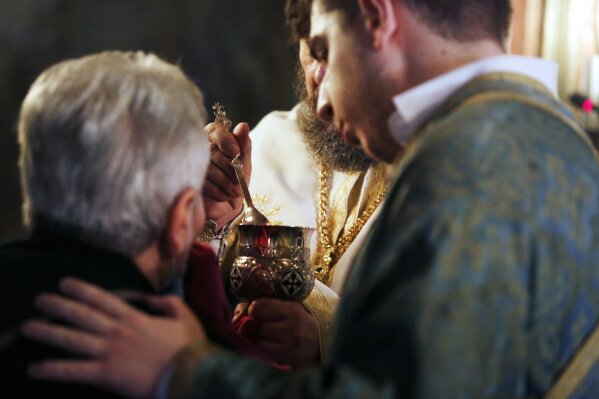 In this Sunday, May 24, 2020, photo, a Greek Orthodox priest uses a traditional shared spoon to distribute Holy Communion during Sunday Mass in the northern city of Thessaloniki, Greece. Contrary t...