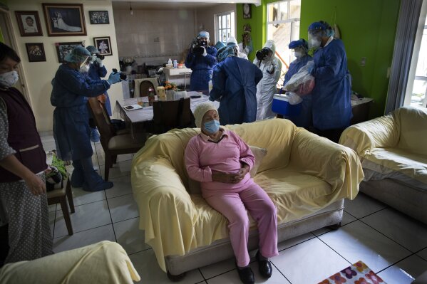 Rebeca Jimenez, 75, sits on a sofa in her home as journalists record health workers preparing to test her for COVID-19, in Mexico City, Wednesday, June 17, 2020. (AP Photo/Marco Ugarte)