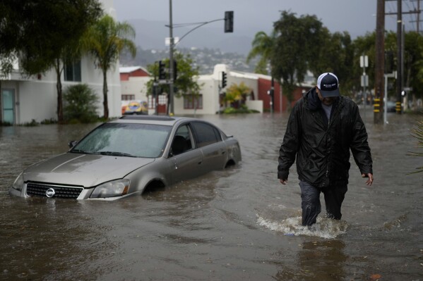 A man walks past a submerged vehicle on a flooded street, Thursday, Dec. 21, 2023, in Santa Barbara, Calif. (AP Photo/Jae C. Hong)