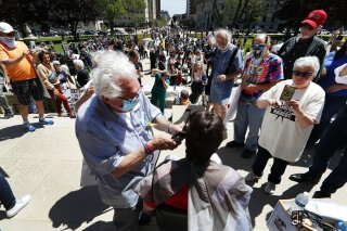 Barber Karl Manke, of Owosso, gives a free haircut on the steps of the State Capitol during a rally in Lansing, Mich., Wednesday, May 20, 2020. Barbers and hair stylists are protesting the state's stay-at-home orders, a defiant demonstration that reflects how salons have become a symbol for small businesses that are eager to reopen two months after the COVID-19 pandemic began. (AP Photo/Paul Sancya)