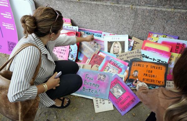 Britney Spears supporters peruse signs on a sidewalk outside the Stanley Mosk Courthouse, Wednesday, Sept. 29, 2021, in Los Angeles. A Los Angeles judge will hear arguments at a hearing Wednesday over removing Spears' father from the conservatorship that controls her life and money and whether the legal arrangement should be ended altogether. (AP Photo/Chris Pizzello)