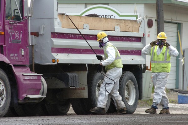 FILE - Unidentified road workers wear protective gear against possible asbestos contamination as they load material from a road resurfacing project in downtown Libby, Mont., April 28, 2011. A health clinic in the Montana town that's plagued by deadly asbestos contamination is liable for almost $6 million in penalties and damages after it submitted hundreds of false claims for government benefits. (AP Photo/Matthew Brown, File)