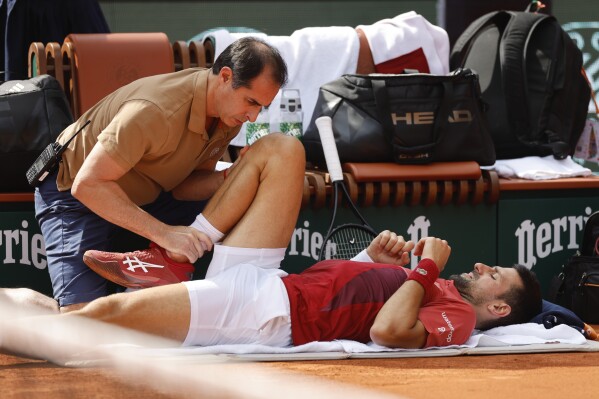 FILE - Serbia's Novak Djokovic receives medical assistance for his right knee during his fourth round match of the French Open tennis tournament against Argentina's Francisco Cerundolo at the Roland Garros stadium in Paris, Monday, June 3, 2024. Novak Djokovic withdrew from the French Open with an injured right knee on Tuesday, June 4, 2024, ending his title defense and meaning he will relinquish the No. 1 ranking. (AP Photo/Jean-Francois Badias, File)