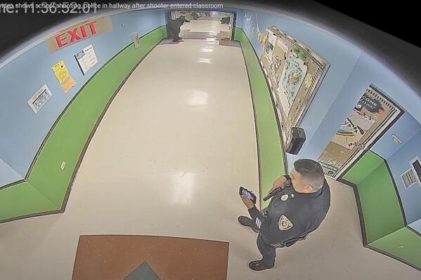 In this photo taken from surveillance video provided by the Uvalde Consolidated Independent School District via the Austin American-Statesman, shows officer Ruben Ruiz, whose wife, Eva Mireles was killed in the shooting, checking his phone in the hallway at Robb Elementary School in Uvalde, Texas, Tuesday, May 24, 2022. (Uvalde Consolidated Independent School District/Austin American-Statesman via AP)/