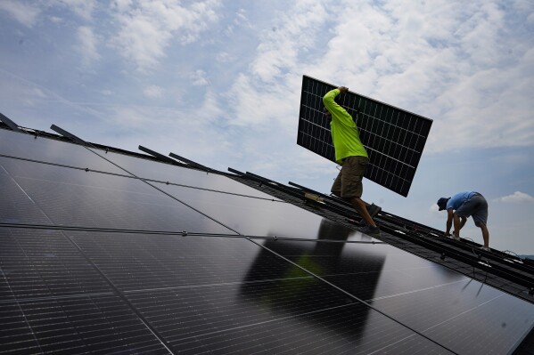 FILE - Nicholas Hartnett, owner of Pure Power Solar, carries a panel as he and Brian Hoeppner, right, install a solar array on the roof of a home in Frankfort, Ky., July 17, 2023. (AP Photo/Michael Conroy, File)