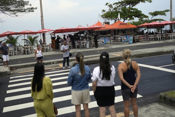 Pedestrians stand across the street from the food and bar kiosk 