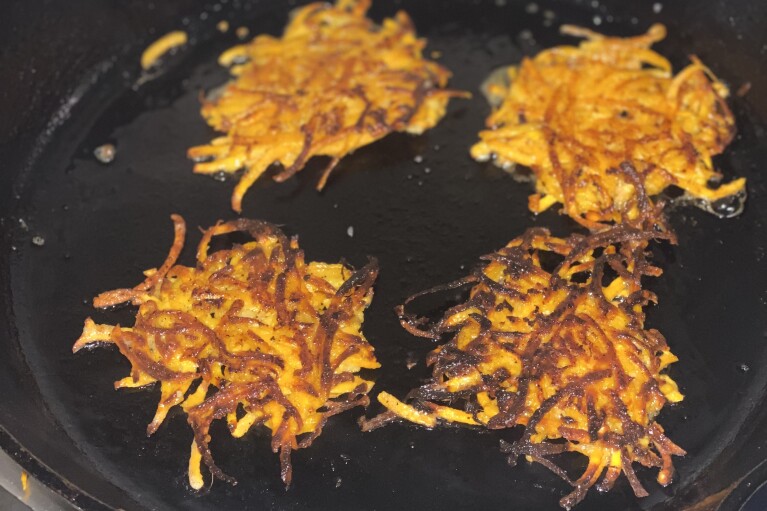 This image provided by Katie Workman shows ginger sweet potato pancakes being fried up in a cast iron skillet. (Katie Workman via AP)