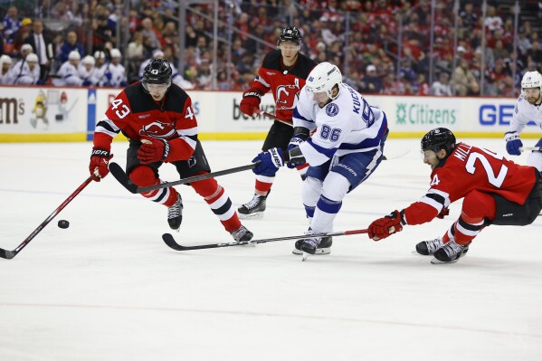 Tampa Bay Lightning right wing Nikita Kucherov (86) shoots the puck against New Jersey Devils defensemen Luke Hughes (43) and Colin Miller (24) during the first period of an NHL hockey game, Sunday, Feb. 25, 2024, in Newark, N.J. (AP Photo/Noah K. Murray)