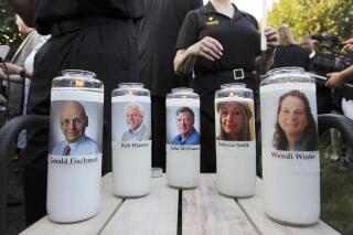 FILE - Photos of five employees of the Capital Gazette newspaper adorn candles during a vigil, June 29, 2018, across the street from where they were slain in the newsroom in Annapolis, Md. The families of victims in the Capital Gazette shooting and some newspaper employees who survived the deadly 2018 attack dismissed civil charges against The Baltimore Sun and Tribune Publishing this week after settling the case. (AP Photo/Jose Luis Magana, File)