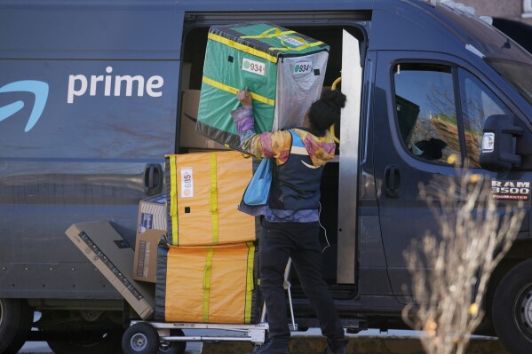 FILE - An Amazon Prime delivery person lifts packages while making a stop at a high-rise apartment building, Nov. 28, 2023, in Denver. Amazon delivered packages to its Prime customers at the fastest speeds ever in 2023, the retailer said Tuesday, Jan. 30, 2024, thanks to better inventory placement, a new regionalization model for shipments and more same-day warehouses. (AP Photo/David Zalubowski, File)