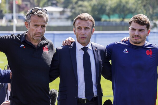 France's President Emmanuel Macron, centre, flanked by France's head coach Fabien Galthie, left, and France's Antoine Dupont during a gathering with the French rugby squad at their base camp's training center in Rueil-Malmaison, outside Paris, Monday, Sept. 4, 2023, ahead of the France 2023 Rugby World Cup. (Ludovic Marin, Pool via AP)