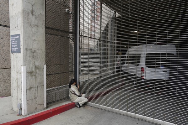 A woman watches as federal immigration authorities arrive with detainees at the Federal Building after conducting operations in Los Angeles, Saturday, June 7, 2025. (AP Photo/Eric Thayer)