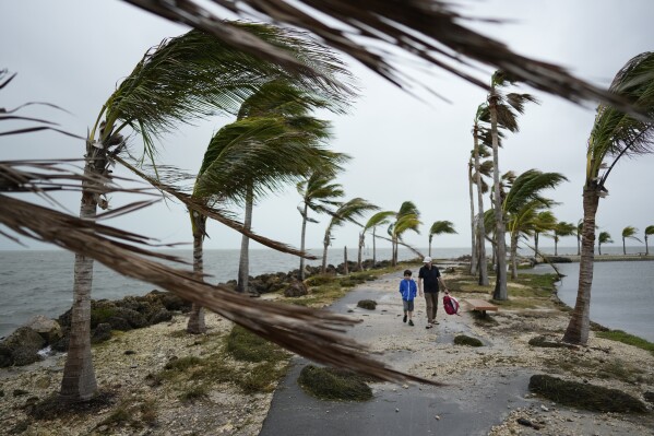 FILE - Bob Givehchi, right, and his son Daniel, 8, Toronto residents visiting Miami for the first time, walk past debris and palm trees blowing in gusty winds, at Matheson Hammock Park in Coral Gables, Fla., Dec. 15, 2023. Nearly all the experts think 2024 will be one of the busiest Atlantic hurricane seasons on record. (AP Photo/Rebecca Blackwell, File)