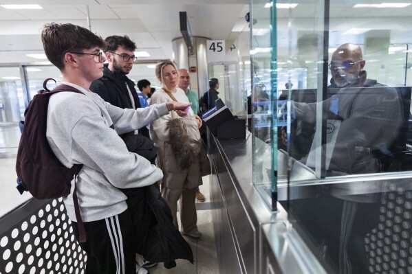 Piet De Staercke, from back right to left, with his wife Jill Bornauw, their eldest son Stan De Staercke, watch their youngest Tuur de Staercke, get screened by a Custom Border Protection officer, right, in the port of entry at Washington Dulles International Airport in Chantilly, Va. Monday, April 1, 2024. The Belgian family of four, used the Mobile Passport Control app, the newest technology in international travel, to ease their way to their port of entry. Within minutes they had bypassed a long line of people waiting at the airport's passport control and were waiting for their luggage. (AP Photo/Manuel Balce Ceneta)