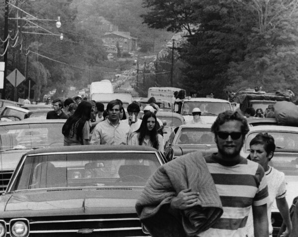 FILE -This Aug. 15, 1969 file photo shows people abandoning their trucks, cars and buses, backed up for 10 miles, as some 200,000 festival goers try to reach the Woodstock Music and Art Festival in Bethel, N.Y.  Woodstock will be celebrated on its 50th anniversary, but it won't be your hippie uncle's trample-the-fences concert. While plans for a big Woodstock 50 festival collapsed after a run of calamities, the bucolic upstate New York site of the 1969 show is hosting a long weekend of events featuring separate shows by festival veterans like Carlos Santana and John Fogerty. (AP File Photo)
