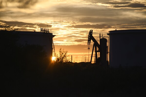 FILE - The sun begins to set behind crude oil tanks and a pumpjack, July 5, 2022, in Midland, Texas. The IEA’s annual world energy outlook, which analyzes the global picture of energy supply and demand, was released Tuesday, Oct. 24, 2023. (Eli Hartman/Odessa American via AP, File)
