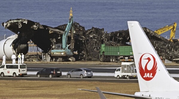 FILE - A removal work, rear, is underway at the site of a planes collision at Haneda airport in Tokyo, on Jan. 5, 2024. The 379 passengers of Japan Airlines Flight JAL-516 didn't expect their plane to burst into flames just as it was about to touchdown at Tokyo’s Haneda airport Tuesday evening. A smaller coast guard Bombardier Dash-8 aircraft, preparing to take off to deliver urgent aid to quake-hit central Japan, was using the same runway when the two collided. The Associated Press collected accounts from witnesses, officials and transcripts of the traffic controls communication. (Kyodo News via AP, File)