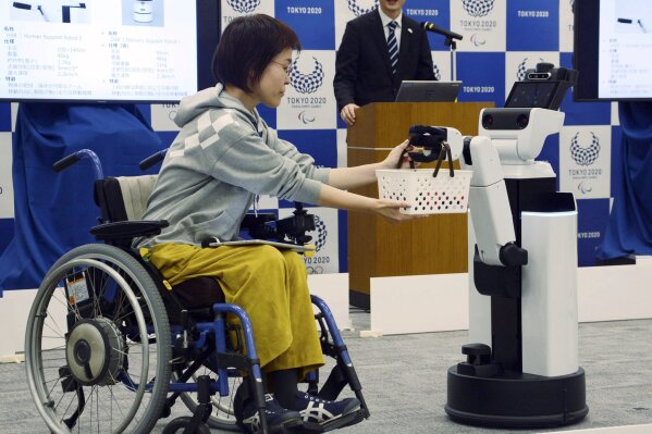 
              A robot passes a basket containing drinks to a woman in wheelchair during an unveiling event in Tokyo Friday, March 15, 2019. Organizers on Friday showed off robots that will be used at the new National Stadium to provide assistance for fans using wheelchairs. (Kyodo News via AP)
            