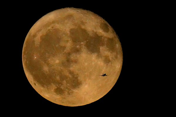 FILE - A commercial airliner flies Northwest across Lake Michigan in front of the "Full Buck" supermoon, the first of four supermoons in 2023, July 3, 2023, in Chicago. The cosmos is offering up a double feature in August: a pair of supermoons. Catch the first show Tuesday night, Aug. 2, as the full moon rises in the southeast. (AP Photo/Charles Rex Arbogast, File)