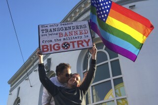 Nick Rondoletto, izquierda, y Doug Thorogood, ambos de San Francisco, ondean una bandera multicolor y sostienen un cartel durante una protesta realizada en San Francisco el miércoles 26 de julio de 2017 para oponerse a una propuesta para prohibir que personas transgénero presten servicio en el ejército de EEUU. (AP Foto/Olga R. Rodriguez, Archivo)