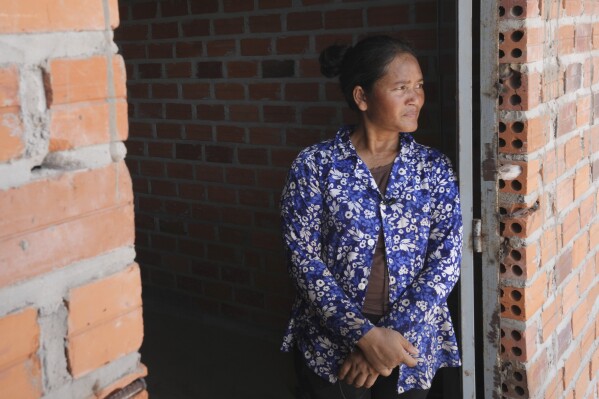 Chhem Hay, 37, stands at a main door of her house under construction at Run Ta Ek village in Siem Reap province, Cambodia, on April 2, 2024. She decided last June to take the opportunity to move from the village where she'd lived since she was a young teenager to the new settlement. Cambodia's program to relocate people living on the famous Angkor archaeological site is drawing international concern over possible human rights abuses, while authorities maintain they're doing nothing more than protecting the UNESCO World Heritage Site from illegal squatters. (AP Photo/Heng Sinith)