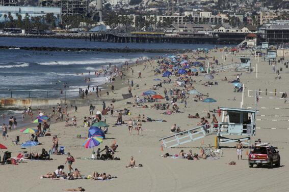 FILE - Swimmers and sunbathers gather at Redondo Beach, Calif., on Presidents Day, Monday, Feb. 15, 2016, as Southern California baked in summer-like heat. California water officials voted, Tuesday, Aug. 2, 2022, to exempt the aging AES Redondo Beach Generating Station, from fines associated with water pollution caused by its operations thorough 2023. It is one of several gas-fired plants that planned to shut down in 2020 until the state required it to stay open throughout 2023 to support the state's energy grid. (AP Photo/John Antczak, File)