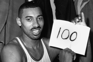 FILE - In this March 2, 1962 file photo, Wilt Chamberlain of the Philadelphia Warriors holds a sign reading "100" in the dressing room in Hershey, Pa., after he scored 100 points, as the Warriors defeated the New York Knickerbockers 169-147. (AP Photo/Paul Vathis, File)