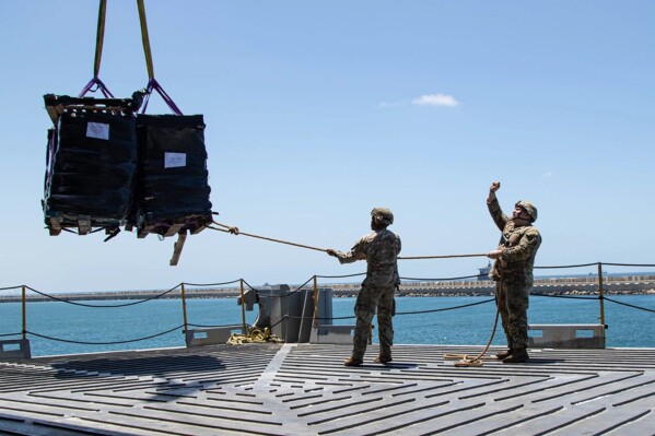 U.S. Army soldiers assigned to the 7th Transportation Brigade (Expeditionary) use a rope to stabilize humanitarian aid while it is lifted by a crane aboard the MV Roy P. Benavidez to support the Joint Logistics Over-the-shore (JLOTS) operation, in the Port of Ashdod, Israel, May 13, 2024. (Staff Sgt. Malcolm Cohens-Ashley/U.S. Army via AP)