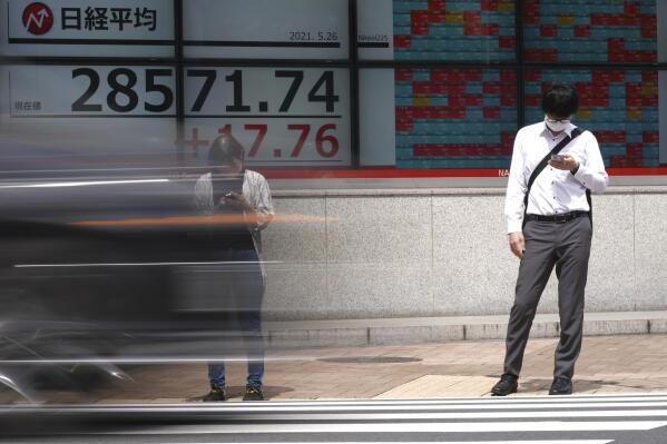 A man and a woman wearing protective masks stand in front of an electronic stock board showing Japan's Nikkei 225 index at a securities firm Wednesday, May 26, 2021, in Tokyo. Asian stock markets rose Wednesday as inflation fears eased and investors looked ahead to U.S. data that are expected to show economic growth accelerating. (AP Photo/Eugene Hoshiko)