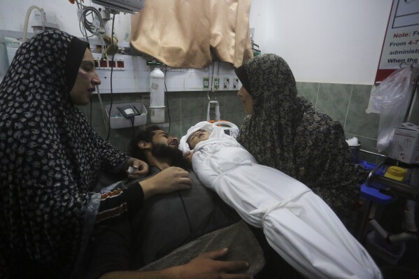 A Palestinian woman shows the body of her grandchild, her father after it was killed in the Israeli bombardment of the Gaza Strip outside a morgue in Rafah, Tuesday, Dec. 19, 2023. (AP Photo/Hatem Ali)