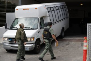 FILE - In this Tuesday, March 19, 2019 file photo, a van carrying asylum seekers from the border is escorted by security personnel as it arrives to immigration court, in San Diego. Scheduling glitches led an immigration judge to deny the Trump administration's request to order four Central American migrants deported because they failed to show for initial hearings Wednesday, March 20, 2019, dealing a setback to a highly touted initiative to make asylum seekers wait in Mexico while their cases wind through U.S. immigration courts. (AP Photo/Gregory Bull, File)