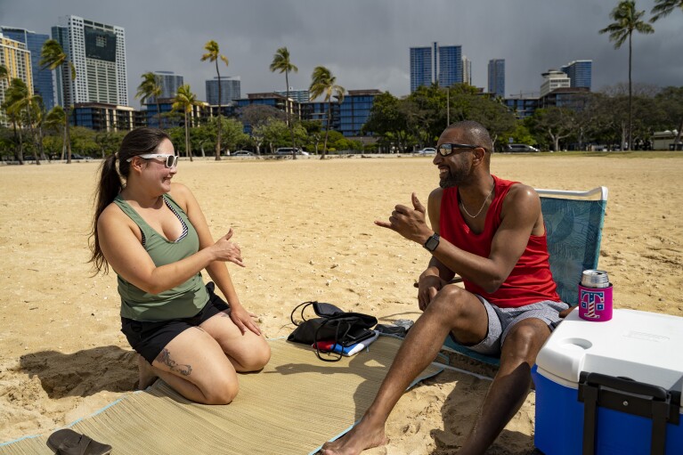 Mignon Walter, left, of Honolulu, exchanges a shaka with Marcus Grayson, of Las Vegas, at Ala Moana Beach on Wednesday, March 6, 2024, in Honolulu, Hawaii. (AP Photo/Mengshin Lin)