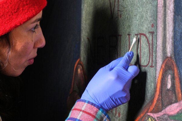 Art conservator Naomi Ruiz uses a cotton swab on a mural by Maxo Vanka that depicts the hand of God handing a tablet to Moses, inside St. Nicholas Croatian Catholic Church in Millvale, Pa., Wednesday, Feb. 19, 2025. (AP Photo/Gene J. Puskar)