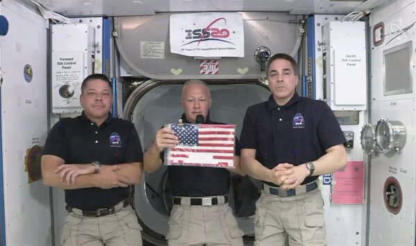 In this image taken from NASA video on Monday, June 1, 2020, NASA astronauts Robert L. Behnken, left, and Chris Cassidy right, listen as commander Douglas Hurley speaks about retrieving the American flag left behind at the International Space Station nearly a decade ago.   (NASA via AP)