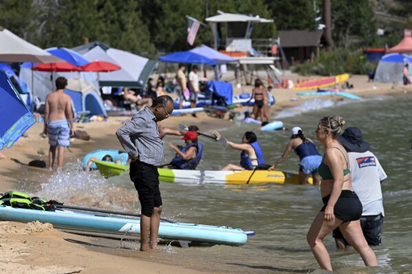 A man wets his feet in the cool water of Lake Tahoe at Lake Tahoe Nevada State Park in Incline Village, Nev., Monday, July 17, 2023. Tourism officials at Lake Tahoe were surprised, and a bit standoffish, when a respected international travel guide included the iconic alpine lake straddling the California line on a list of places to stay away from this year because of the harmful ecological effects of “over-tourism.” (AP Photo/Andy Barron)