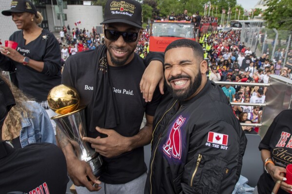 ARCHIVO - Kawhi Leonard de los Toronto Raptors, al frente a la izquierda, sostiene su trofeo MVP mientras posa con el rapero/productor Drake mientras celebran durante el desfile del campeonato de baloncesto de la NBA del equipo en Toronto, el 17 de junio de 2019. Así como la banda sonora de una película ayuda a los espectadores a seguir la acción de la narrativa a través de cada giro de la trama, el hip-hop ha hecho lo mismo con el baloncesto a través de la NBA.  Drake ha sido embajador mundial del equipo de su ciudad natal, los Toronto Raptors, desde 2013 y, a menudo, se lo ve al margen interactuando con entrenadores y jugadores.  (Frank Gunn/The Canadian Press vía AP, archivo)