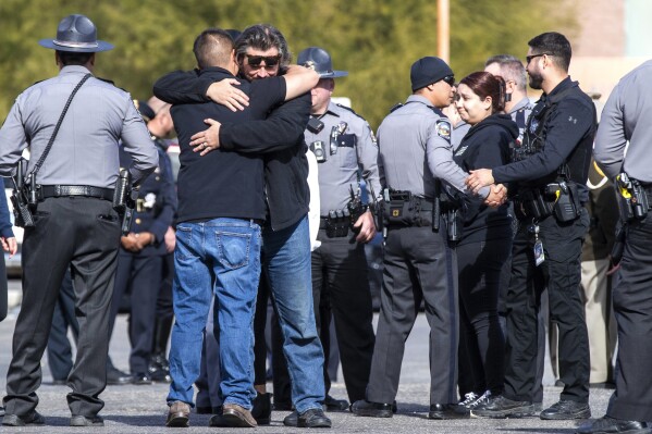 Nevada State Police and other law enforcement officers embrace in the parking lot after the body of a state trooper was taken into the Clark County Coroner's Office in Las Vegas, Thursday, Nov. 30, 2023. Two troopers who were assisting a motorist early Thursday morning were hit by a vehicle and killed, according to Nevada State Police. (Steve Marcus/Las Vegas Sun via AP)