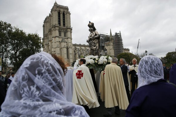 Catholic clergymen and pilgrims take part in an emotional procession with the statue of the Virgin Mary rescued from the April blaze past the fire-ravaged Notre Dame Cathedral to celebrate the Assumption of the Virgin in Paris, Thursday, Aug. 15, 2019. (AP Photo/Francois Mori)