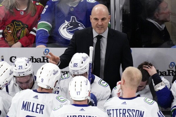 FILE - Vancouver Canucks head coach Rick Tocchet, top, talks to players during the third period of an NHL hockey game against the Chicago Blackhawks in Chicago, Sunday, Dec. 17, 2023. The Canucks won 4-3. In completing his first full season behind the Canucks bench, Tocchet is not alone among his coaching contemporaries in providing their respective teams a spark. Of the 16 teams entering the NHL playoffs this weekend, seven feature coaches who are in their first full year or hired as midseason replacements.(AP Photo/Nam Y. Huh)