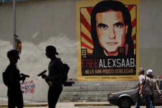 FILE - In this Sept. 9, 2021 file photo, pedestrians walk near a poster asking for the freedom of Colombian businessman and Venezuelan special envoy Alex Saab, and that reads in Spanish "They haven't been able to bend him," in Caracas, Venezuela. Venezuela’s government quietly offered in 2020 to release imprisoned Americans, the so-called Citgo 6 along with two former Green Berets tied to a failed cross border raid, in exchange for the U.S. letting go Saab, a key financier of President Nicolás Maduro, who was extradited to Miami in Oct. 2021. (AP Photo/Ariana Cubillos, File)