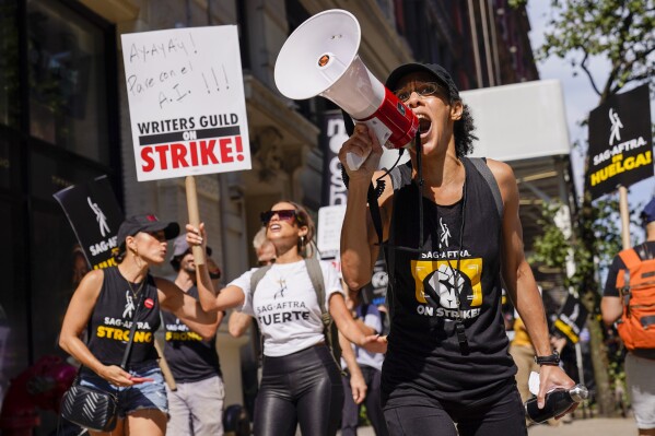 A strike captain, right, leads the chants as strikers walk a picket line outside Warner Bros., Discovery, and Netflix offices in Manhattan, Friday, Aug. 18, 2023. The WGA and SAG-AFTRA held a joint Latine Picket, presented by the WGAE Latine Writers Salon, the WGAW Latinx Writers Committee, and the SAG-AFTRA National Latino Committee. (AP Photo/Mary Altaffer)
