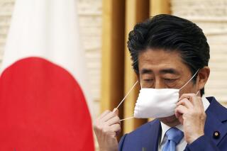 FILE - In this May 4, 2020, file photo, then Japanese Prime Minister Shinzo Abe removes a face mask before speaking at a press conference at his official residence in Tokyo. Nearly 83 million, or nearly one-third, of unpopular cloth masks that were too small and old-fashioned and remembered as "Abenomasks” by the public last year were unused and mothballed in a private storage for a hefty rent. (AP Photo/Eugene Hoshiko, File)