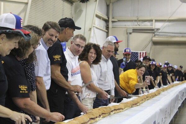 Volunteers help assemble the 150-foot-long (45.7-meters-long) bologna sandwich at the Lebanon Area Fair on Tuesday, July 25, 2023 in Lebanon, Pa. Every footlong “bite” was sponsored at $100 per foot. The money was donated to Lebanon County Christian Ministries and their efforts to help people dealing with food insecurity in the Lebanon Valley. ( Daniel Larlham Jr. /Lebanon Daily News via AP)