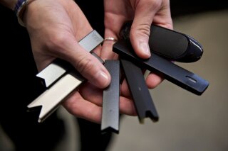FILE - In this April 16, 2019, file photo, a researcher holds vape pens in a lab at Portland State University in in Portland, Ore. As of October 2019, experts who examined lung tissue from 17 patients say lung damage reported in people who use e-cigarettes and other vaping devices looks like chemical burns similar to what you’d see in people exposed to poisonous gases. (AP Photo/Craig Mitchelldyer, File)