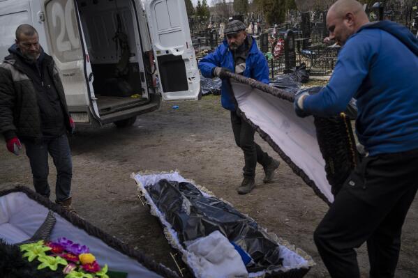 Cemetery workers prepare the coffin for a person killed during the war with Russia, as dozens of black bags containing more bodies of victims are seen strewn across the graveyard in the cemetery in Bucha, in the outskirts of Kyiv, Ukraine, Monday, April 11, 2022. (AP Photo/Rodrigo Abd)
