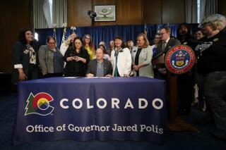FILE- Colorado Governor Jared Polis, center, signs three bills that enshrine protections for abortion and gender-affirming care procedures and medications during a ceremony with bill sponsors and supporters on April 14, 2023, in the State Capitol in Denver. Colorado is promising not to enforce its new ban on unproven treatments to reverse medication abortions until state regulators go through a process to determine if they should be allowed. (AP Photo/David Zalubowski, File)