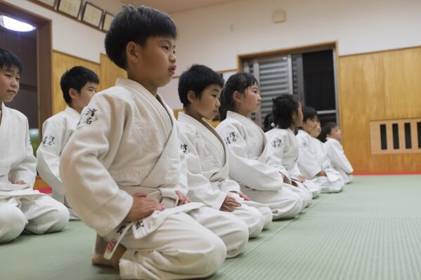 Elementary school students, front row, sit straight at the end of their judo practice as older students, back row, join to start their lesson at Hamana Dojo in Oiso town, west of Tokyo on Oct. 1, 2020. Japan is the home of judo, and the 19th-century martial art is sure to get more attention at home than any other sport at next year’s postponed Tokyo Olympics. But it’s also drawing unwanted scrutiny over widespread allegations of violence, and accompanying injuries and abuse. (AP Photo/Hiro Komae)